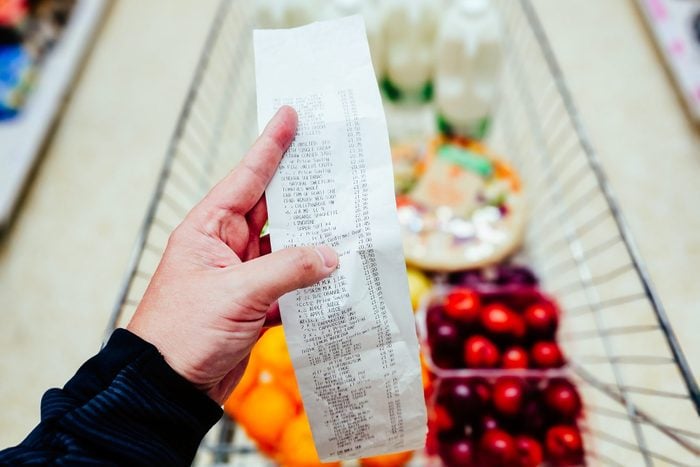 hand holding supermarket receipt over basket full of groceries in the background
