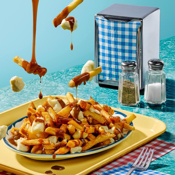 Styled photo of poutine dripping onto a plate, on a teal background with a napkin holder, salt and pepper.
