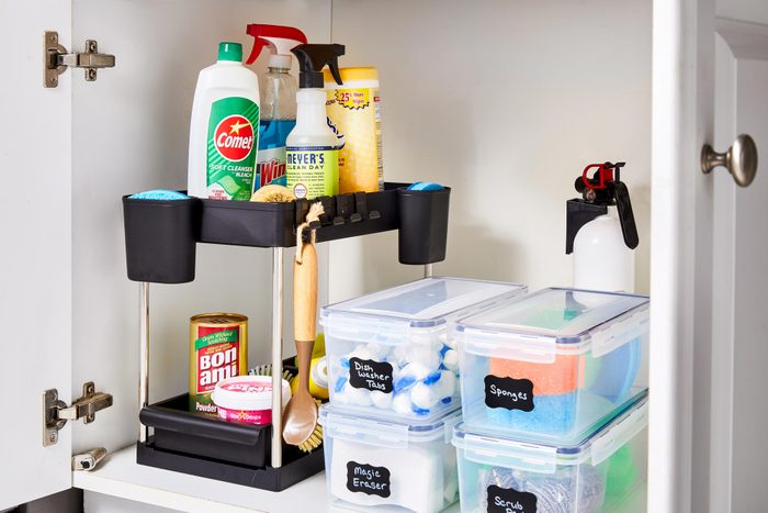 cleaning supplies in the cabinet under a kitchen sink organized with shelving