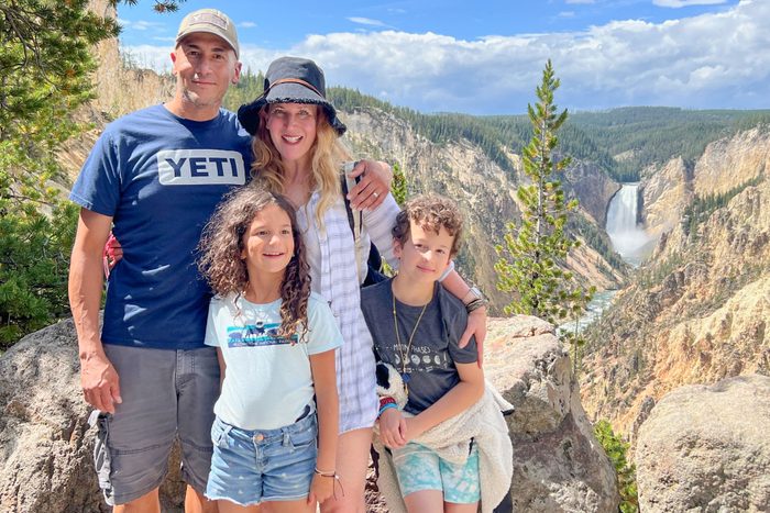 author, Anne Fritz, on vacation with her husband and kids in yellowstone national park posing with a waterfall in the background