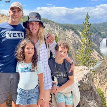 author, Anne Fritz, on vacation with her husband and kids in yellowstone national park posing with a waterfall in the background