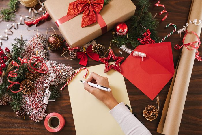 Hand writing a Christmas card on a table with presents and present wrapping supplies