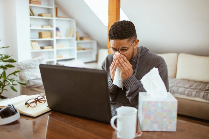 Young African American man blowing his nose while working on laptop