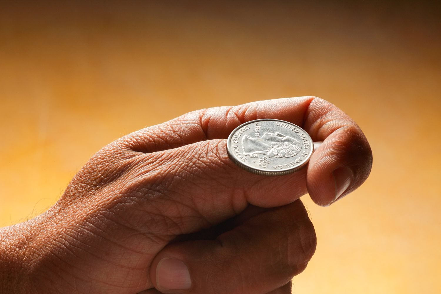 Mans Hand Pictured with a Quarter on his thumb and index finger, indicating a coin flip is about to happen, landing on heads or tails when it lands