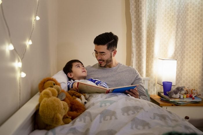 father and son are cuddled up together in bed whilst the father is reading a bedtime story.