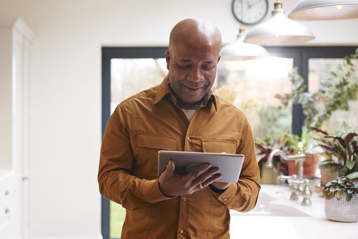 Man At Home In Kitchen Reading On Digital Tablet