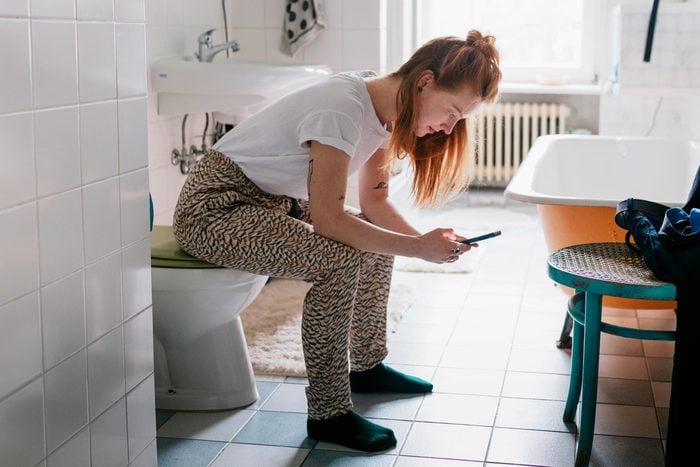 girl sitting on toilet with her phone