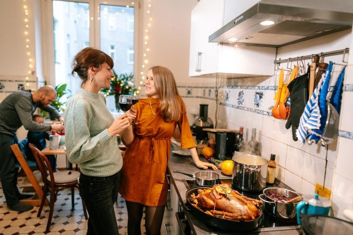 Two women having wine and talking while cooking Christmas meal in kitchen