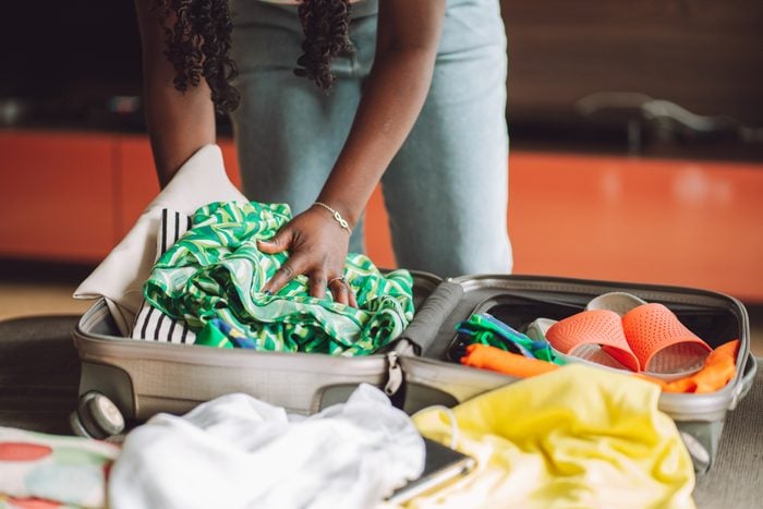 African American woman stacking clothes and shoes into bag case, trying to pack hand luggage