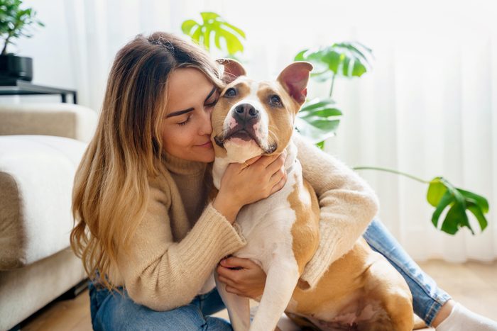 Portrait of blonde young woman hugging happy Pitbull Terrier dog at home