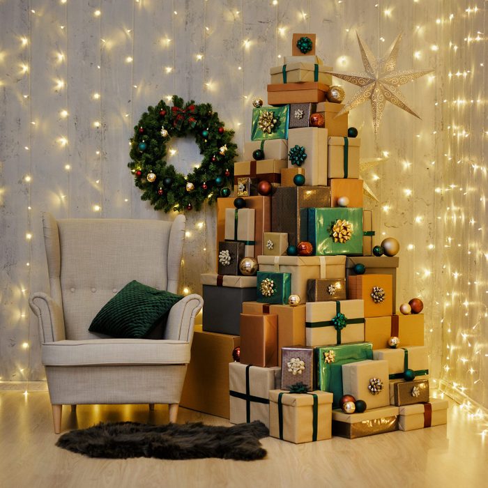 Home interior with armchair, led lights and Christmas gift boxes laid out in the shape of a Christmas tree