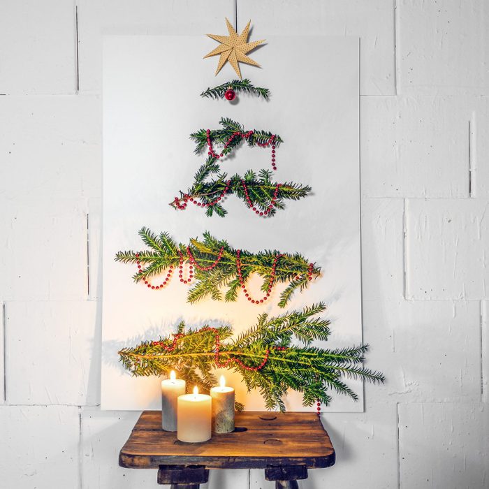 Homemade Christmas tree alternative, white cardboard plate with fir branches and decoration leaning against the wall on an old wooden stool with candles, copy space