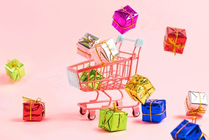 miniature shopping cart with colorful gifts boxes falling all around; light red background