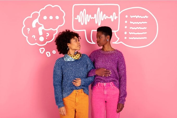 Two African American women linking arms and looking at each other standing against a pink wall, conversation doodles