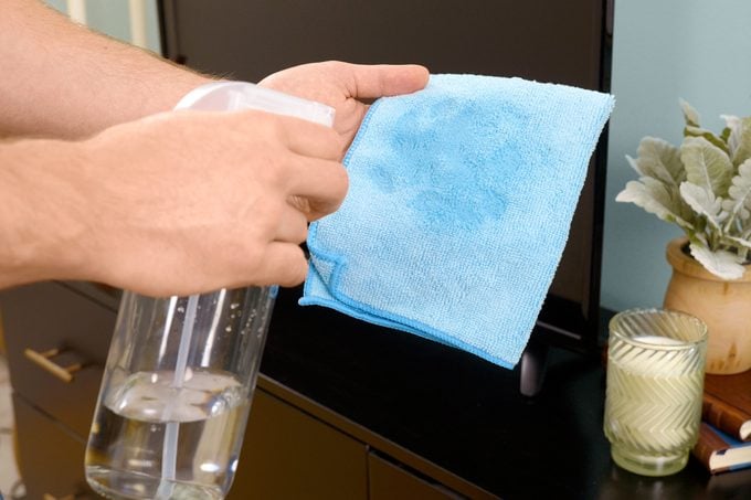 cleaning flat screen tv with blue cloth and a spray bottle