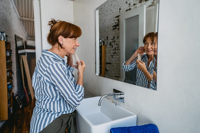 Senior red headed woman adjusting hair in bathroom