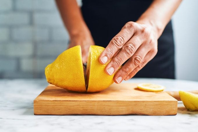 hand cutting a lemon in half on a cutting board