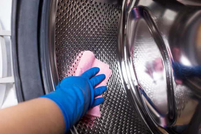hand wearing blue gloves wiping down the inside of a washing machine with a pink cloth