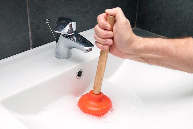 hand using an orange plunger in bathroom sink