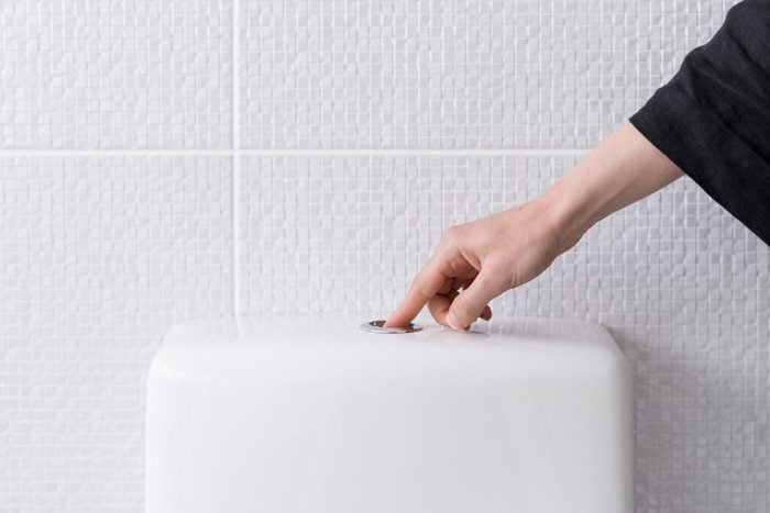 Woman's hand pushing button and flushing toilet
