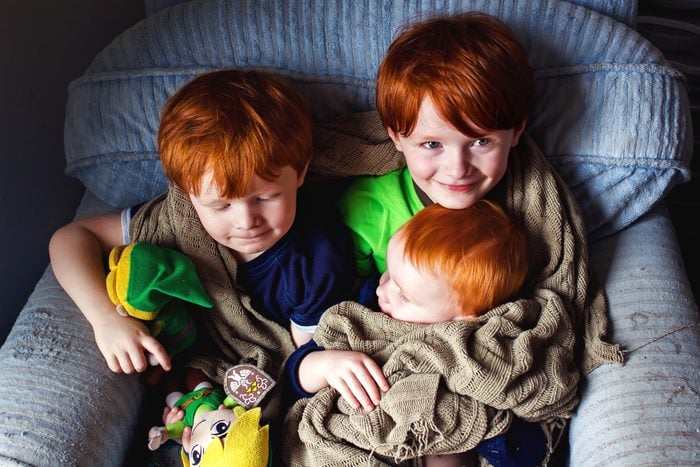three young redheaded brothers sitting together in a blue arm chair