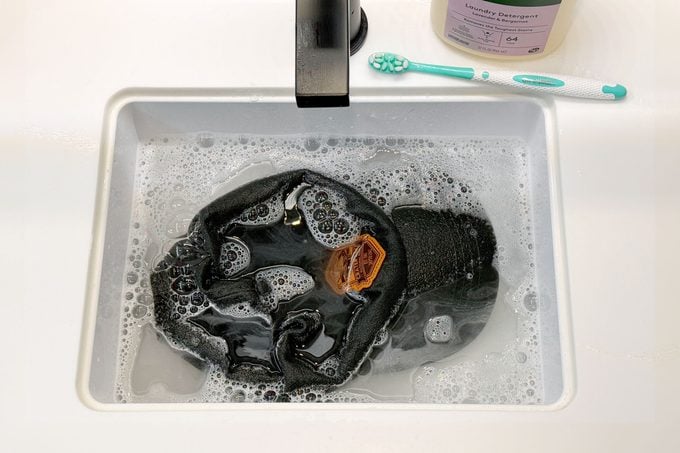 baseball hat in a bathroom sink with detergent and a toothbrush to the side