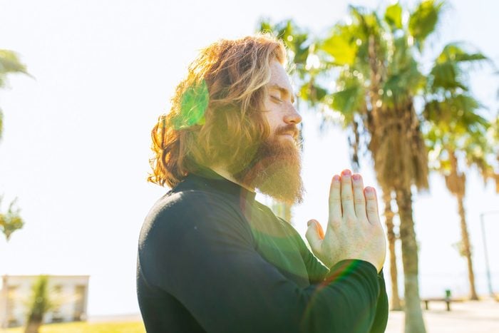 red haired Man With Long Beard Wear Black Sporty Suit Doing Yoga Meditation outdoors on Sunny Beach