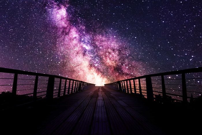 silhouette of a bridge path that leads to a purple cosmic sky with stars