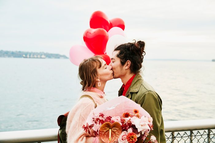 Couple holding heart shaped balloons kissing while exploring city