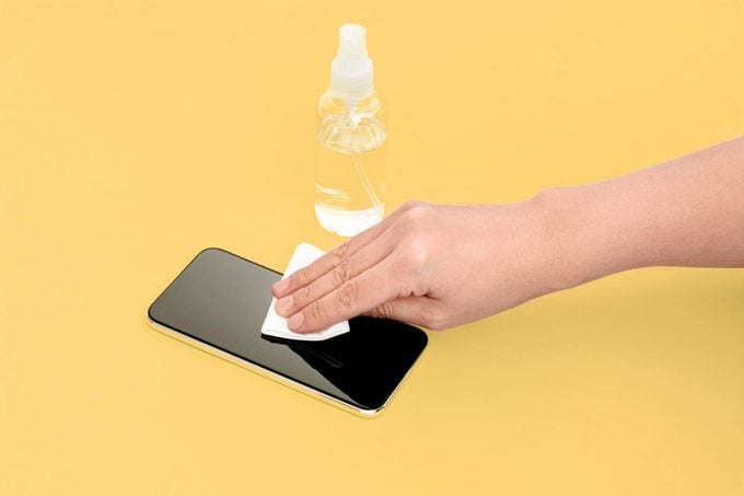 wiping phone with cloth on a yellow background and a small spray bottle in the background