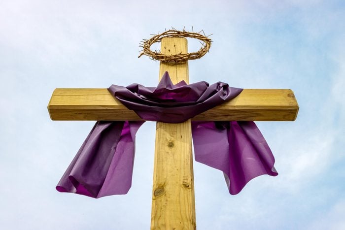 Wooden cross with crown of thorns and purple Lent cloth outside on sunny day