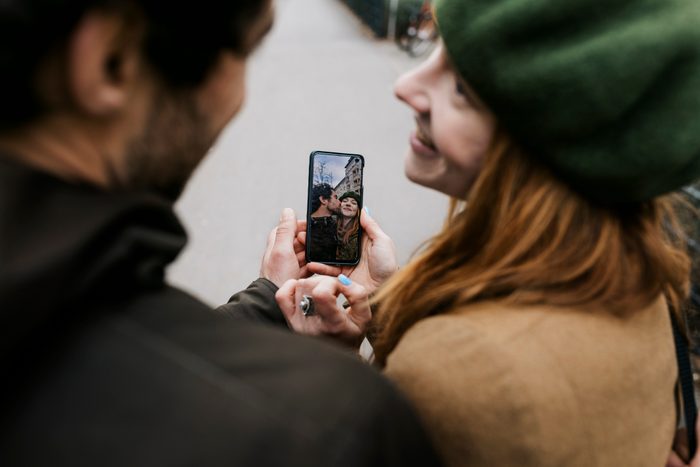 Couple Smiling While Looking At Selfies On Smartphone Together