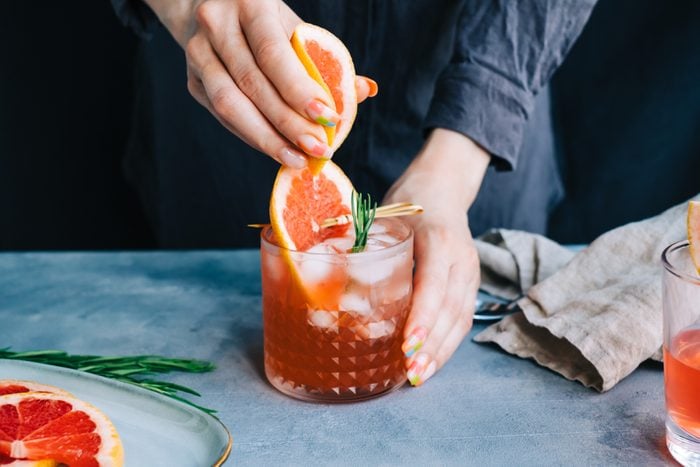 Female bartender hand squeezes juice from fresh grapefruitÂ in cocktail lemonade with ice and rosemary.