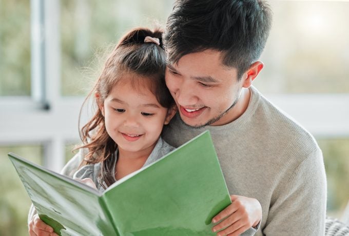 Shot of of a little girl sitting on her father's lap with a book