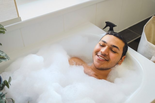 High angle view of smiling man taking bath in bathtub at home