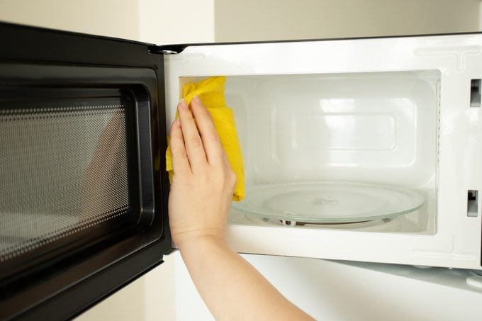 a woman's hand washes a microwave with a rag, cleanliness and hygiene in the kitchen