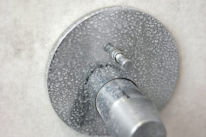 Dirty calcified shower mixer tap, faucet with limescale on it, plaque from hard water, Chrome plated shower, close up photo. Bathroom with grey tiles interior.