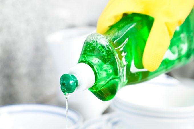 hand with yellow rubber gloves holding bottle of green dish soap