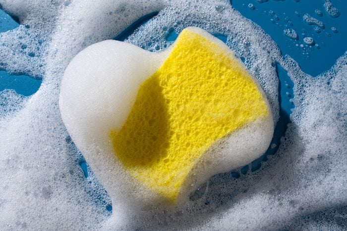 Yellow Sponge With White Soap Foam Scrubbing on Blue Background