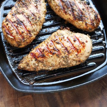 three cooked chicken breasts in a skillet on a wood table