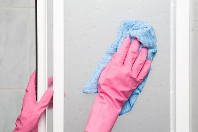 Employee's hand in rubber protective glove with rag washing and polishing a shower doors. Maid or housewife cares about house. Spring general or regular clean up. Commercial cleaning company concept.