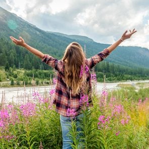 Cheering Woman Open Arms At Sunrise In Wild Flowers Field By The River