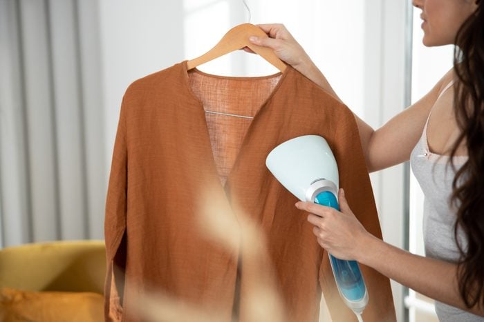 Young lady refreshing shirt with clothes steamer