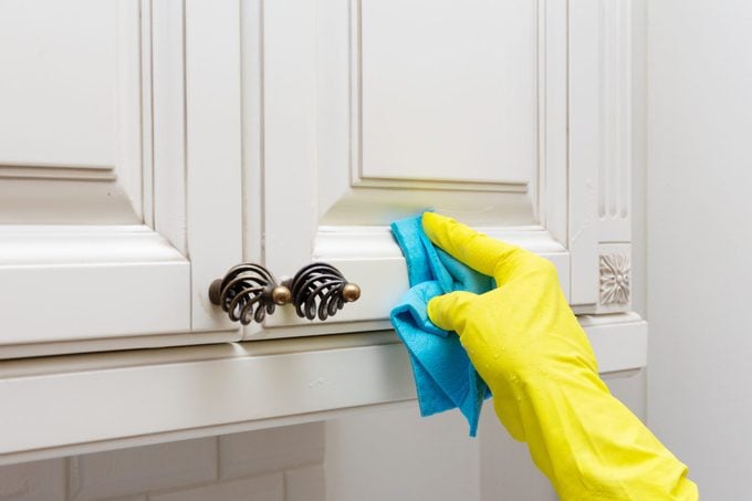 Female hand in a yellow glove with a blue napkin or rag wipes and washes the surface of the kitchen furniture