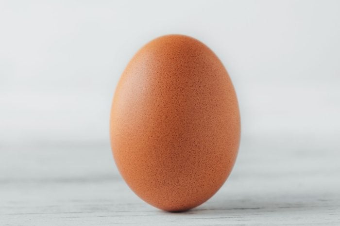 Brown chicken egg stands on wooden table on white background.