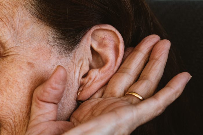 A senior woman holding her ear, trying to hear