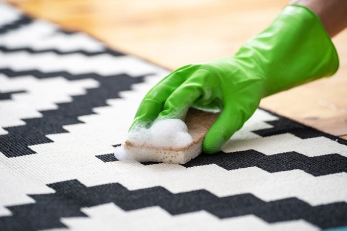hand in glove clean rug with sponge and detergent