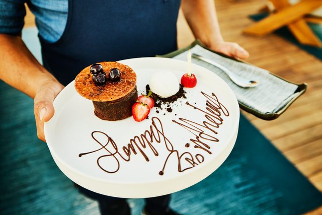 Close up shot of waiter holding desert plate decorated with Happy Birthday
