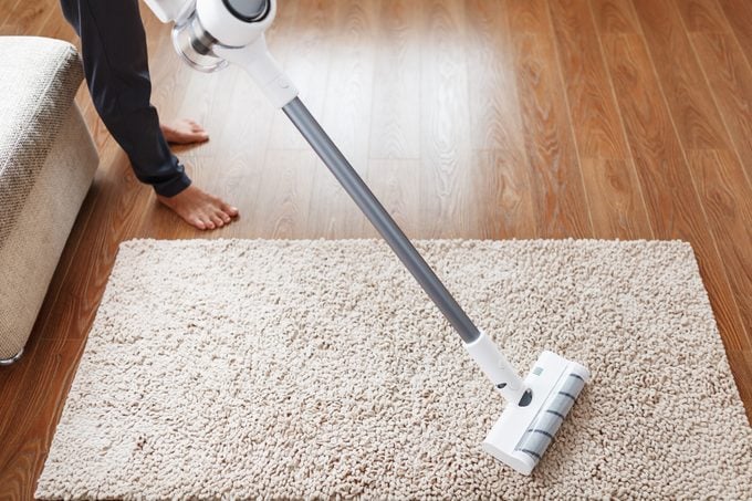 A cordless vacuum cleaner cleans the carpet in the living room with the bottom of the legs.