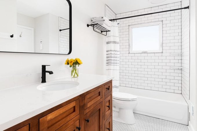 A farmhouse bathroom with a wood cabinet and subway tile shower.